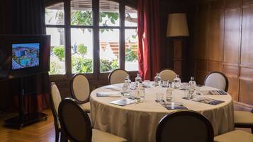 A conference room with a round table, chairs, a television, and a window with curtains.