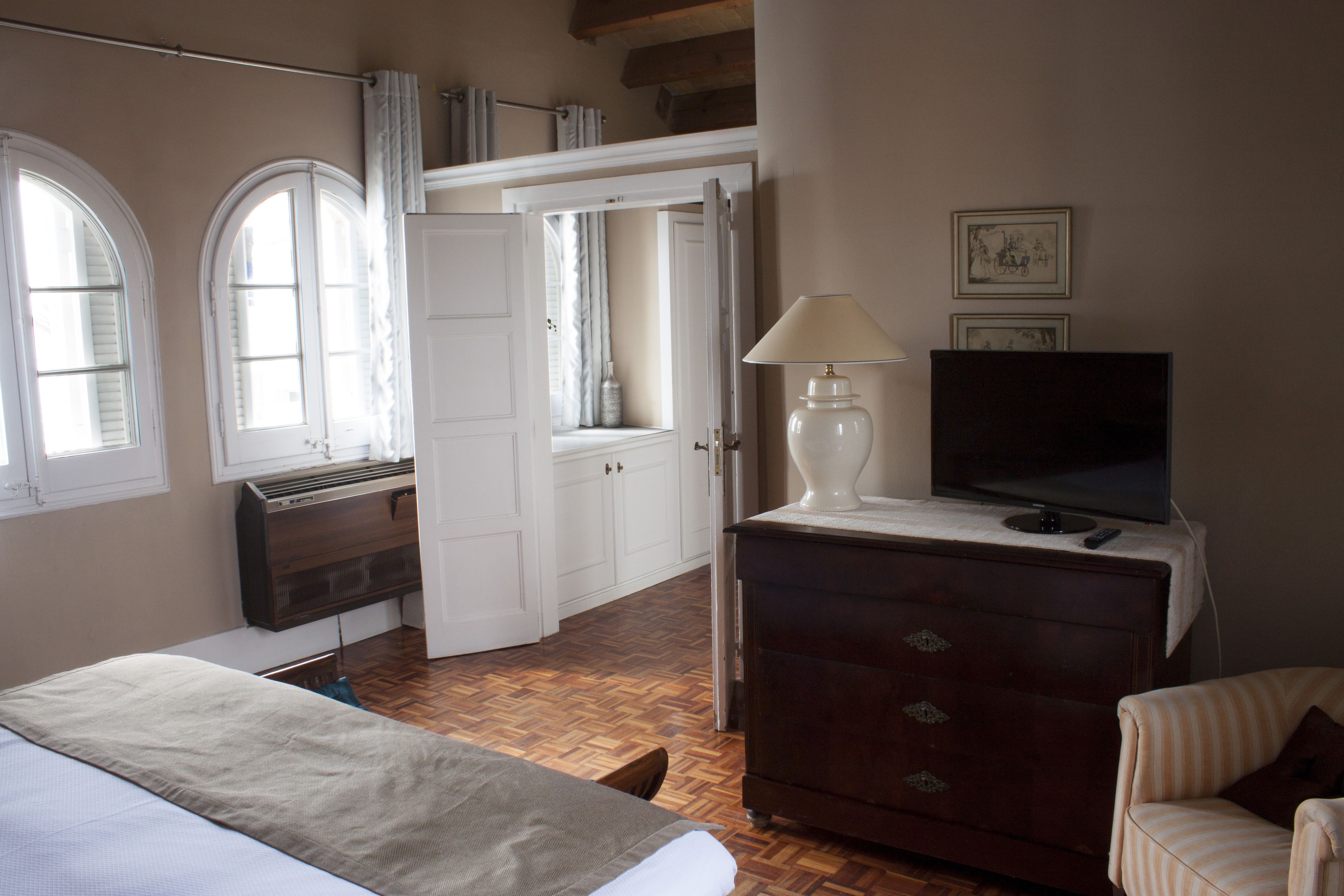 Un dormitorio con cama, cómoda, televisor y ventana con cortinas.