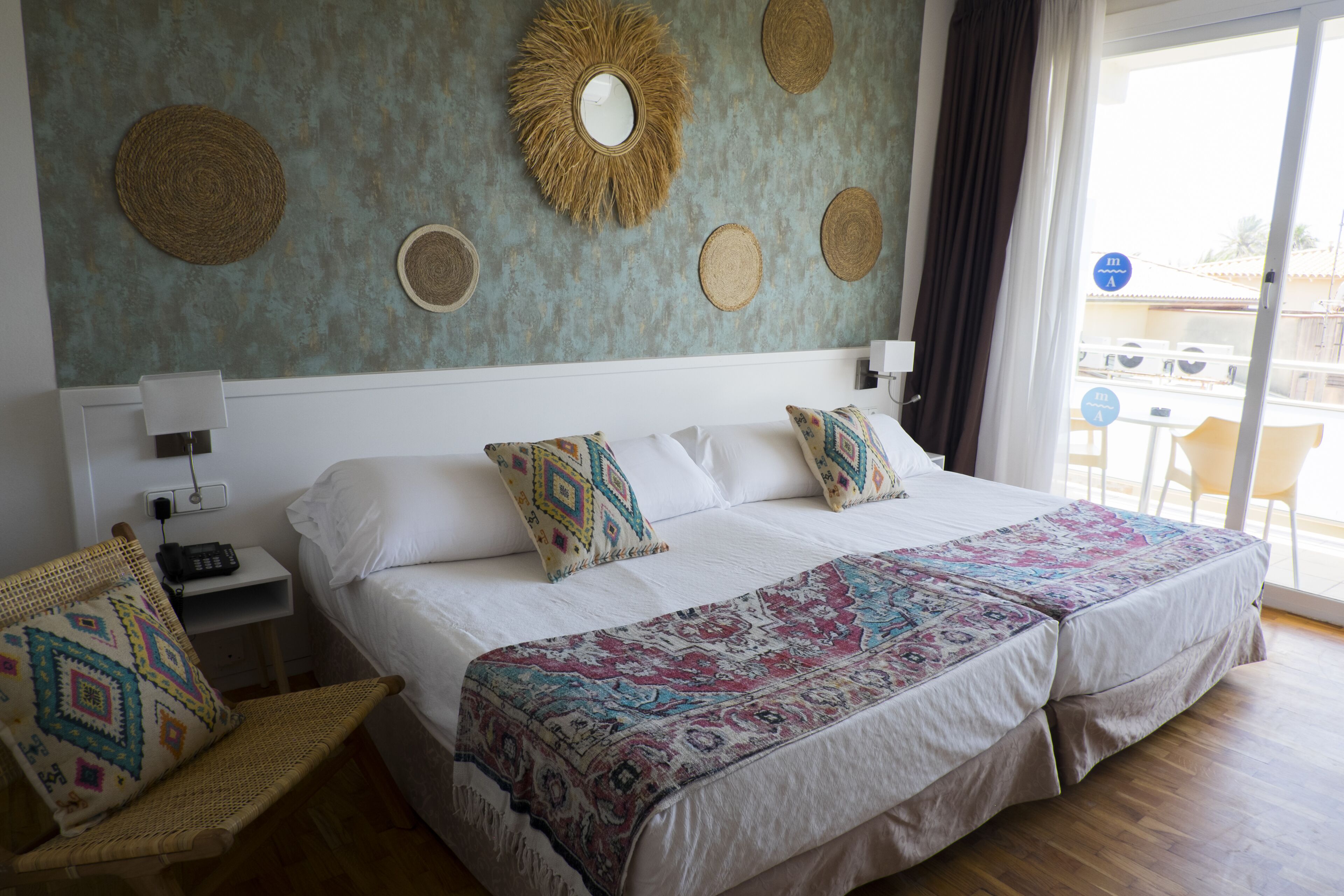 Habitación de hotel con una cama grande, dos mesitas de noche, una silla y vistas al exterior.