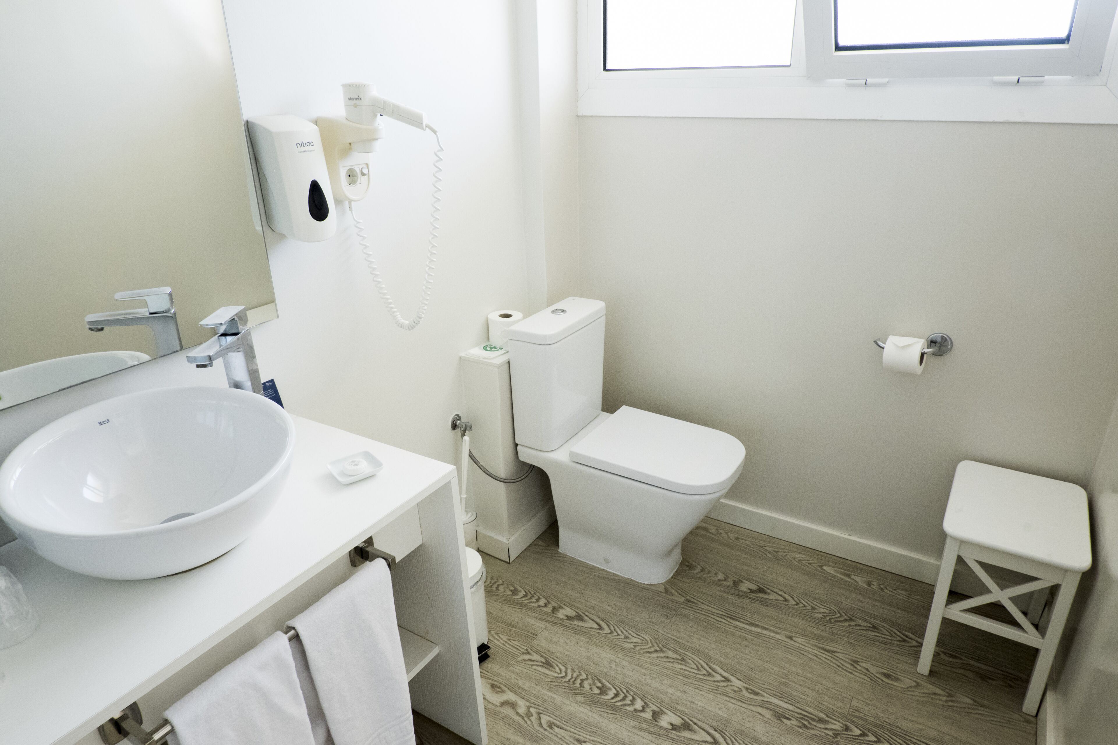 A bathroom with a white sink, toilet, and a small white stool.
