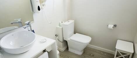 A bathroom with a white sink, toilet, and a small white stool.