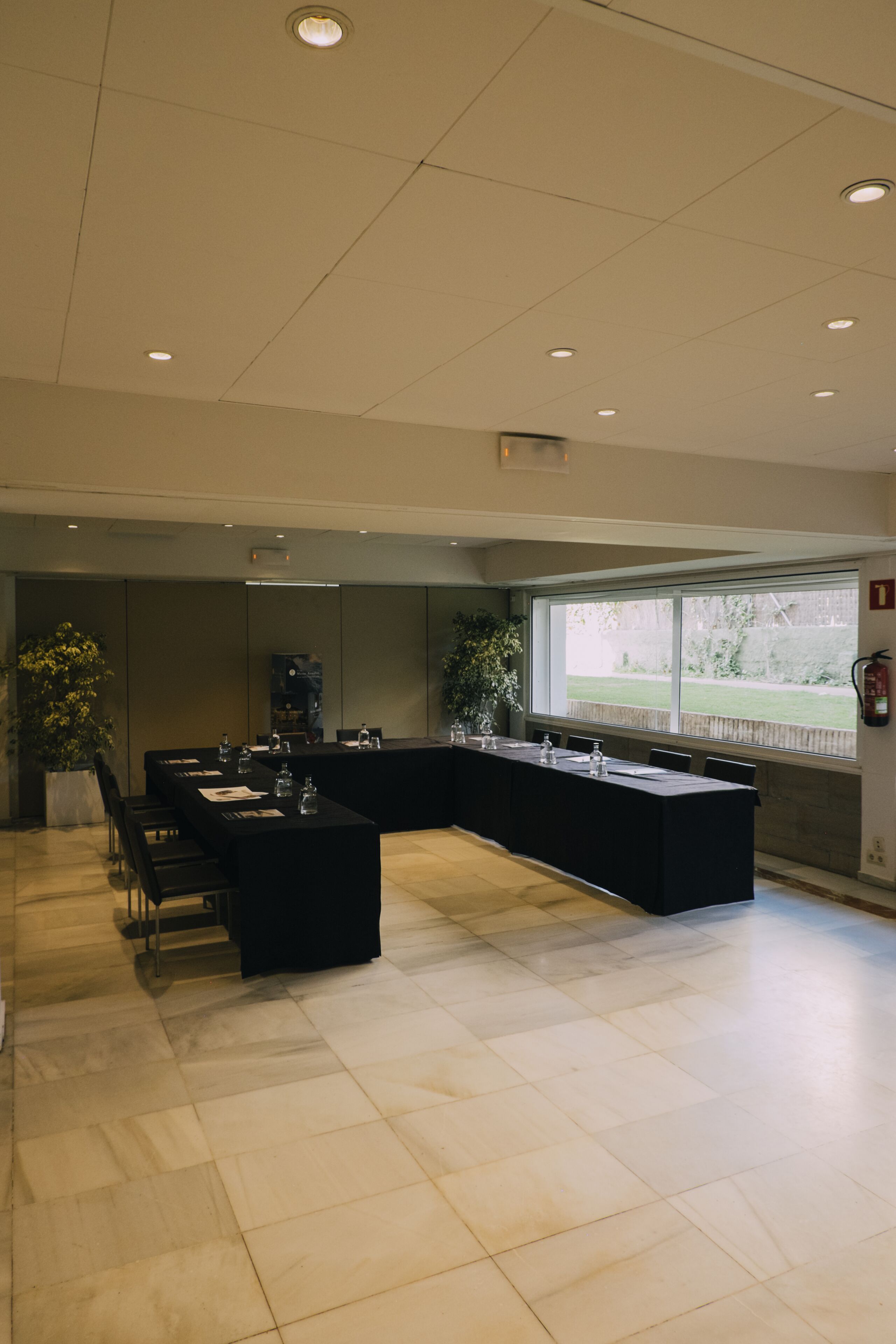 A modern conference room with a long table, chairs, and a large window providing a view of the outdoors.