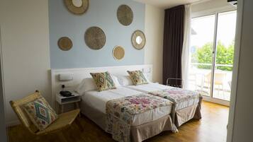 Hotelkamer met twee bedden, een stoel, een nachtkastje met telefoon en uitzicht op het omliggende landschap door een schuifdeur.