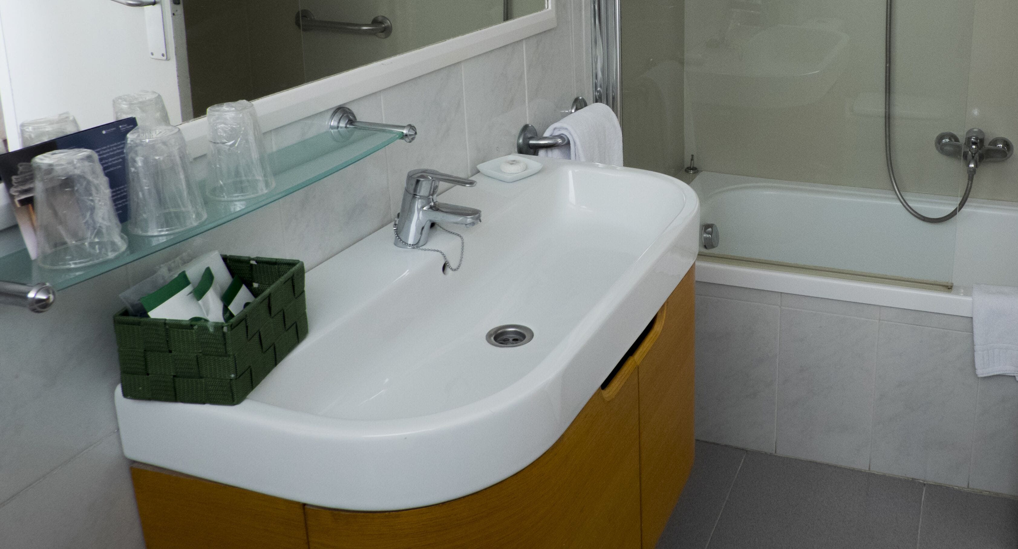 Un baño con un lavabo blanco, una repisa de vidrio con artículos de aseo y una zona de ducha.