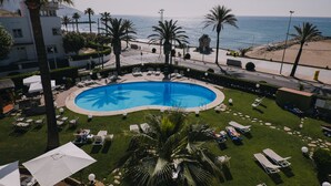 A pool with a blue mosaic design, surrounded by lounge chairs and umbrellas, with a view of the beach and ocean. - Hotel Subur Maritim (Sitges)