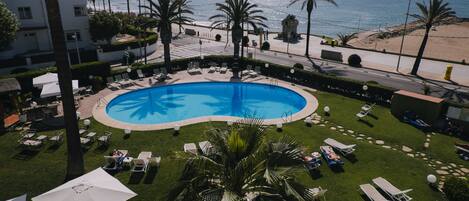 A pool with a blue mosaic design, surrounded by lounge chairs and umbrellas, with a view of the beach and ocean.