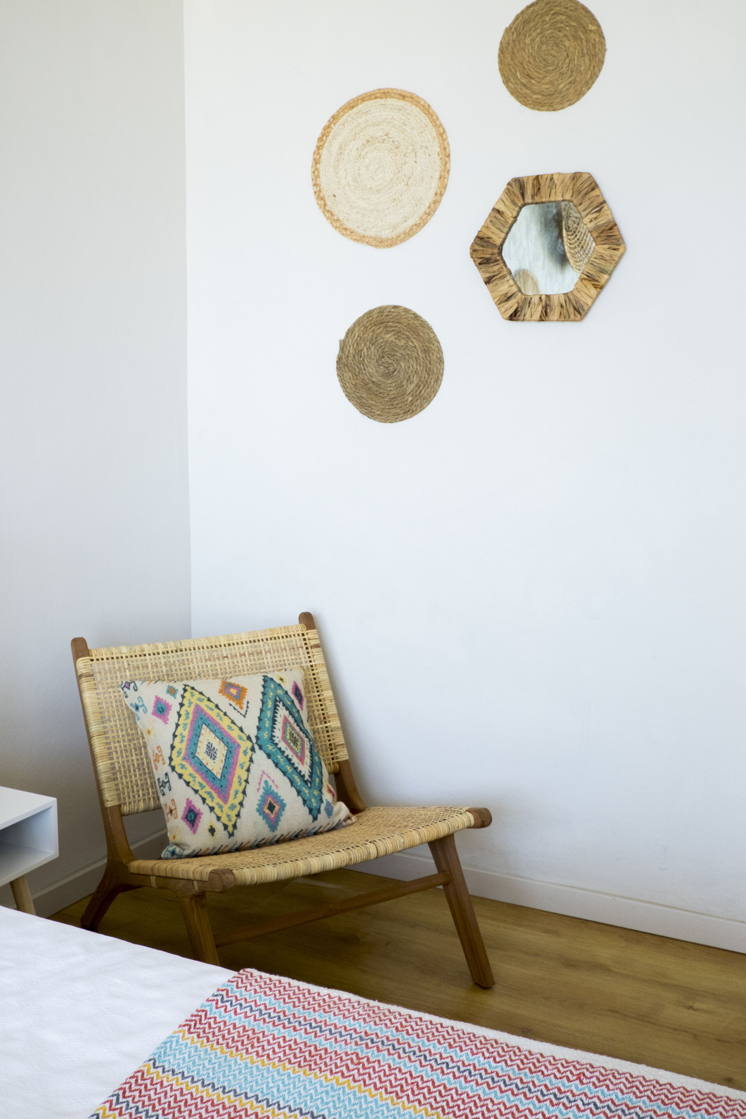 A room with a wicker chair, a colorful woven rug, and three woven wall decorations.