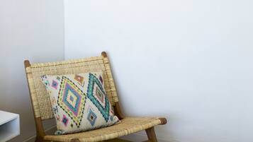 Une pièce comprenant un fauteuil en osier, un tapis coloré tissé et trois éléments décoratifs en tissu accrochés au mur.