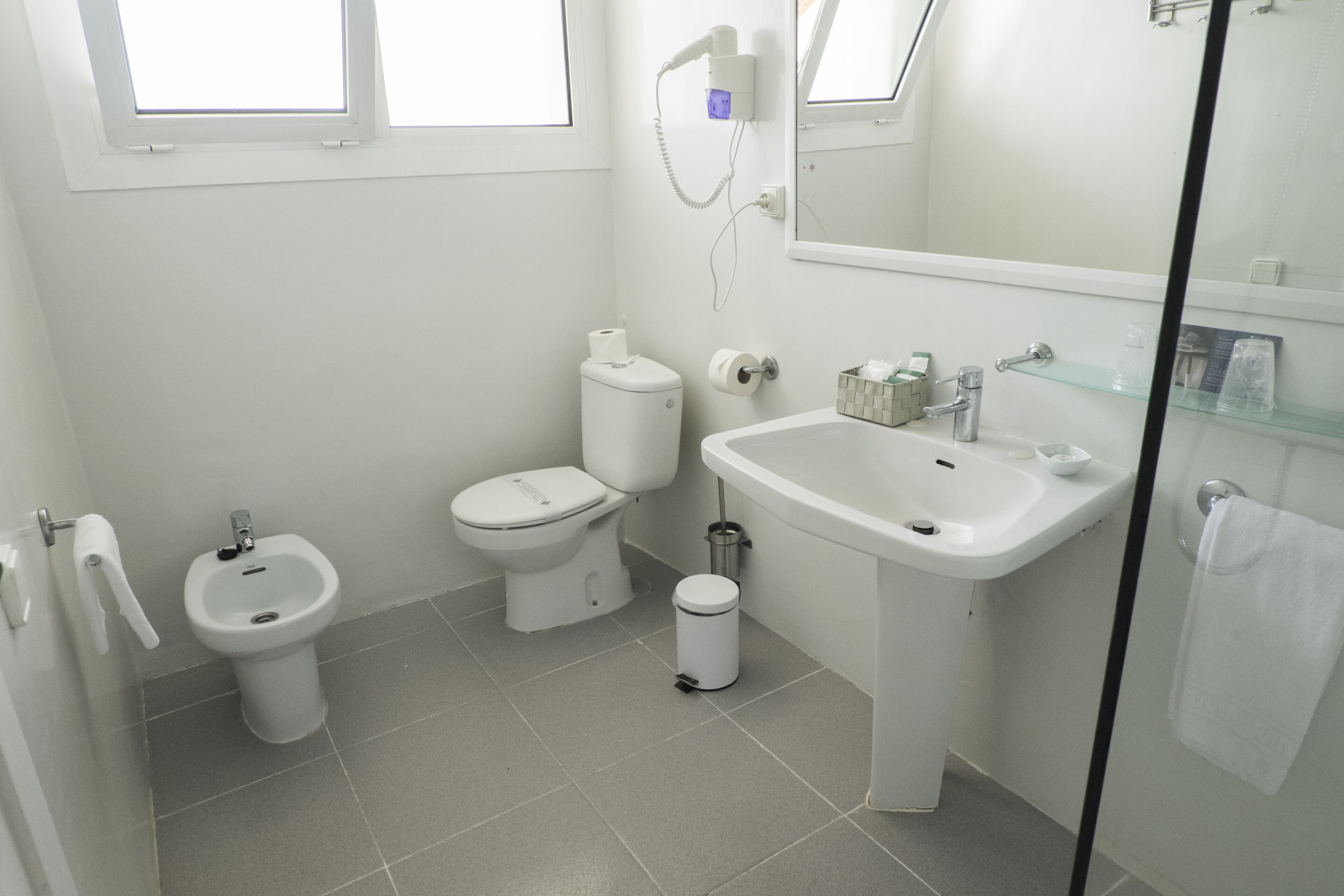 A modern bathroom with a toilet, bidet, sink, and glass shower enclosure.