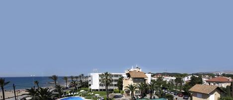 A hotel with a swimming pool, palm trees, and a view of the sea.