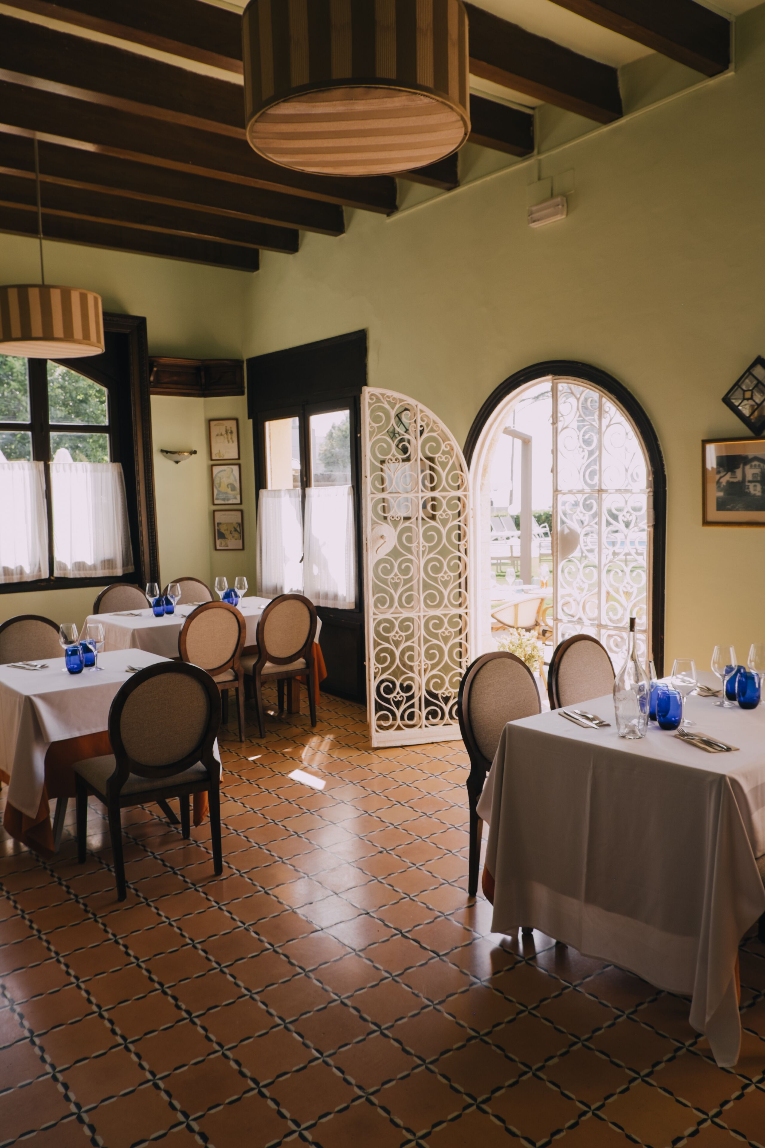 Un comedor con mesas dispuestas para una comida, que presenta un suelo de baldosas y vigas de madera en el techo.