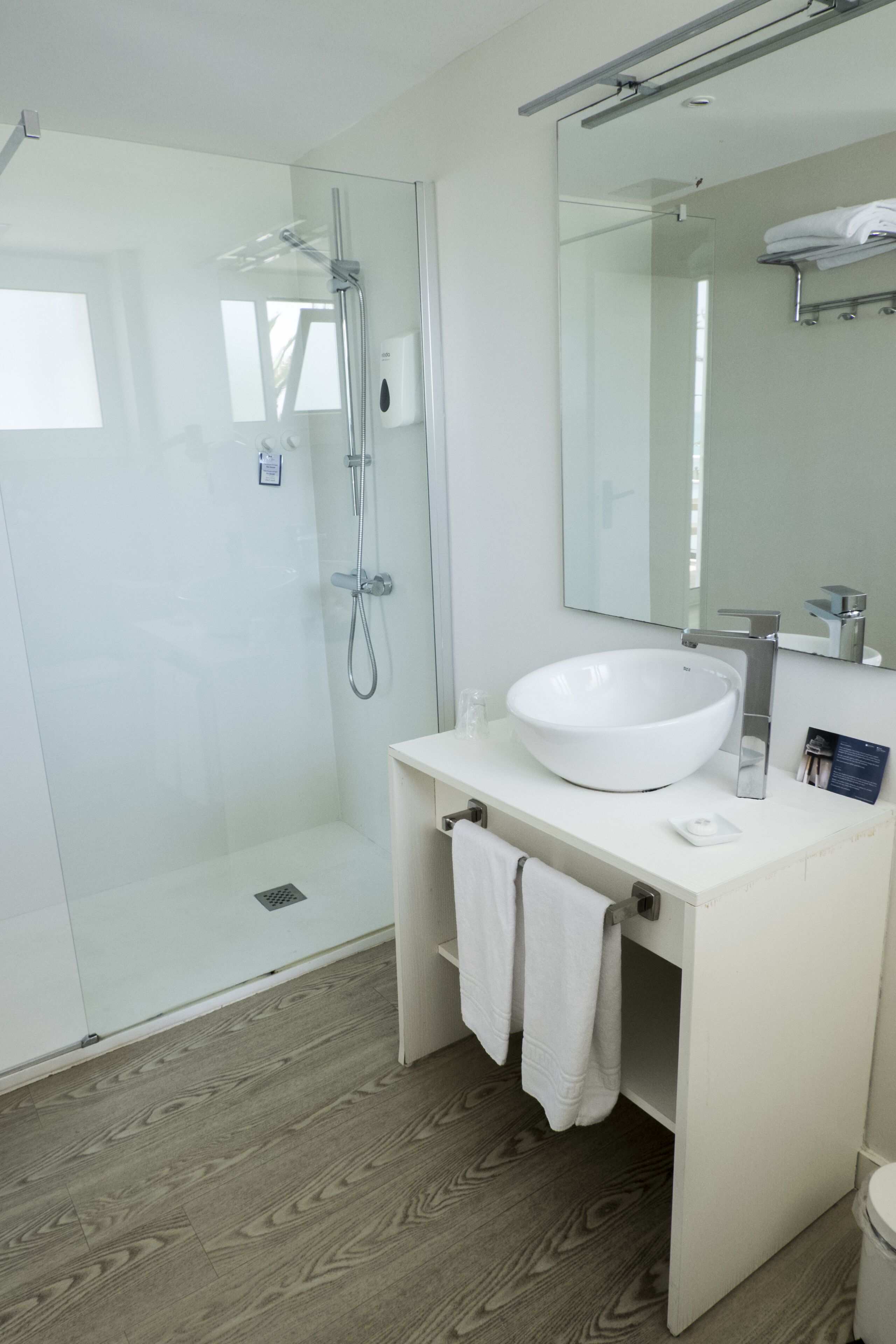 A modern bathroom with a glass-enclosed shower, a white sink, and a large mirror.
