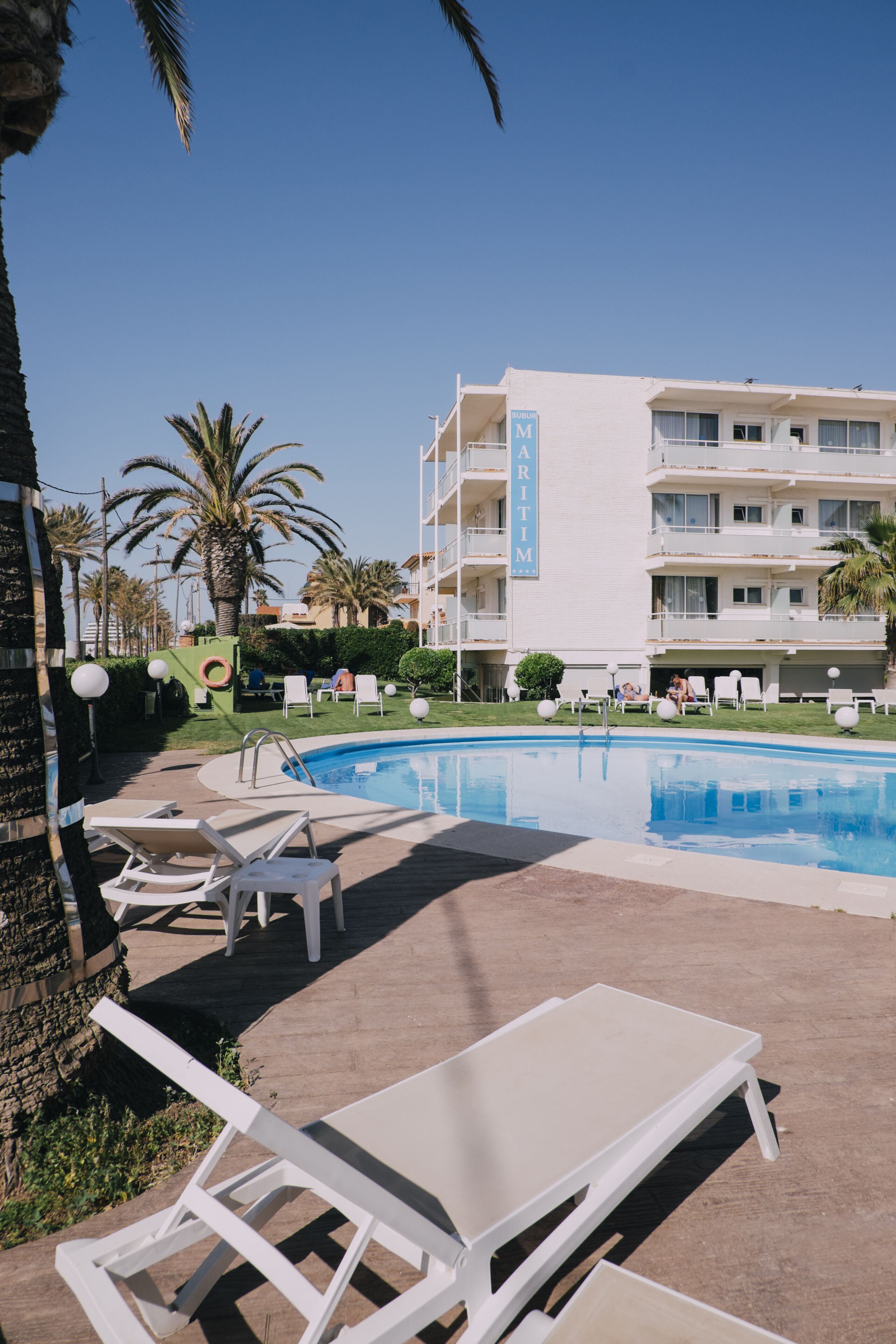 Un hôtel doté d’une piscine, de chaises longues et de palmiers.