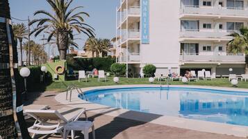 Un hôtel doté d’une piscine, de chaises longues et de palmiers.