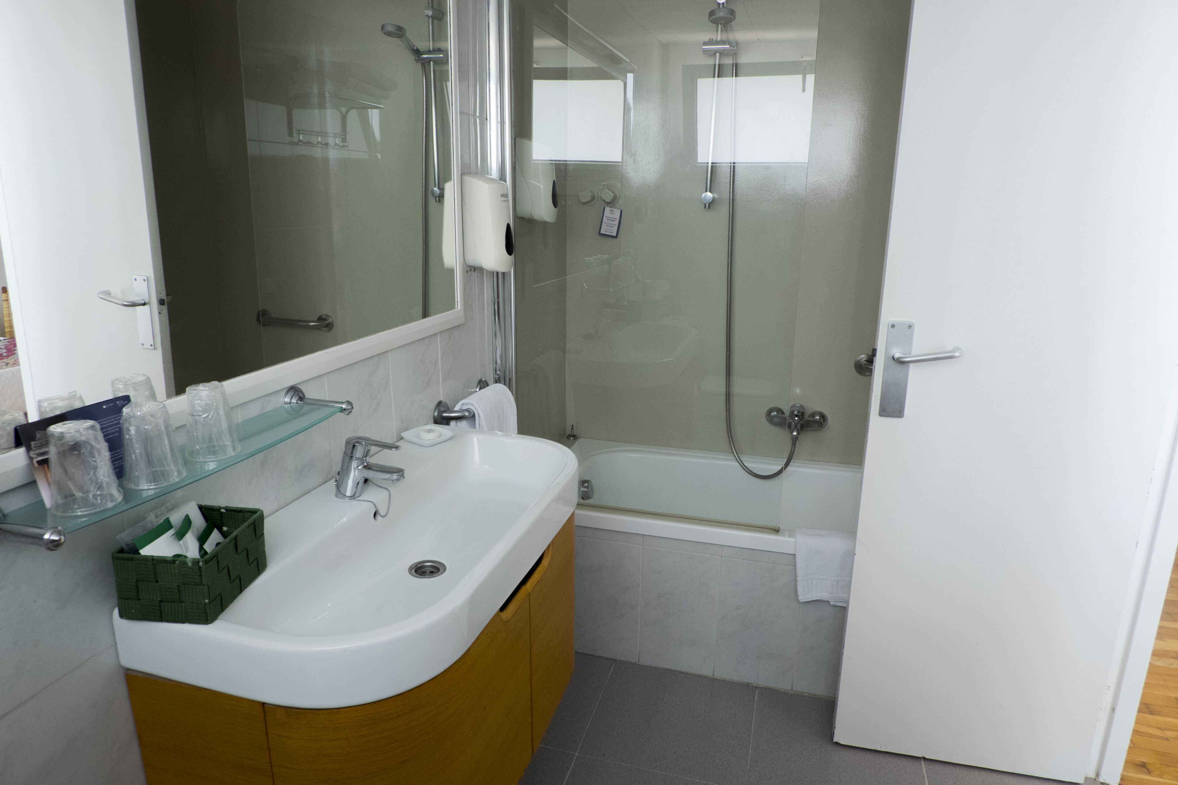 Een moderne badkamer met een douchecabine van glas, een witte wastafel met houten kastje en een glazen plank met toiletartikelen.
