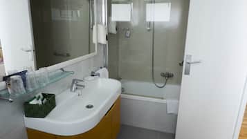 Een moderne badkamer met een douchecabine van glas, een witte wastafel met houten kastje en een glazen plank met toiletartikelen.