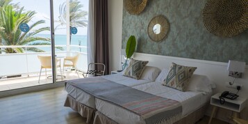 A hotel room with a large bed, a nightstand with a phone, a chair, a view of the ocean, and a balcony with chairs.