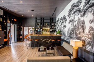 Uma área de bar moderna com balcão de madeira, banquetas e um mural com árvores na parede.