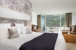 Quarto de hotel moderno com uma cama grande, um sofá e uma varanda com vista panorâmica.