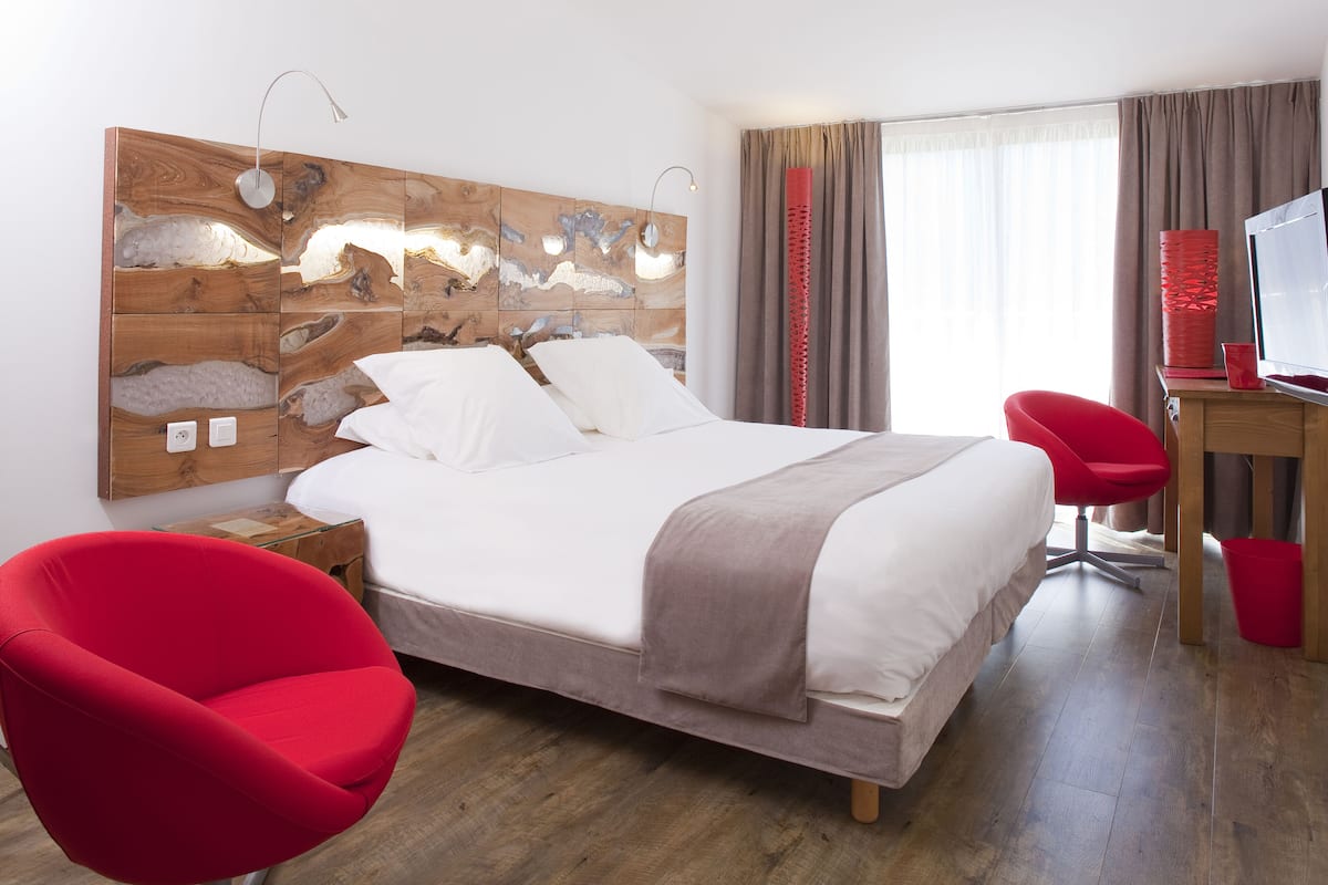 Una habitación de hotel moderna con cabecera de madera, cama grande, escritorio con silla roja y televisión.