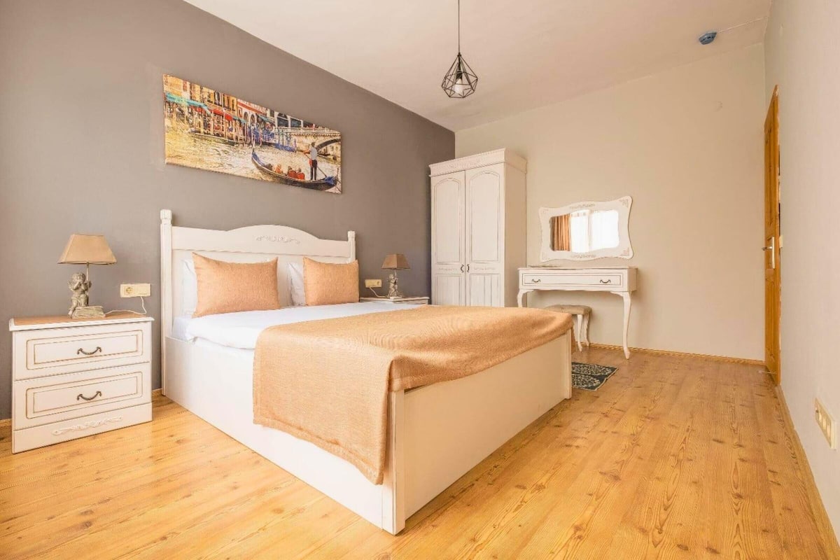 Ein Schlafzimmer mit einem Bett, Nachttischen, einem Schreibtisch, einem Stuhl, einem Kleiderschrank und einem Bild an der Wand.