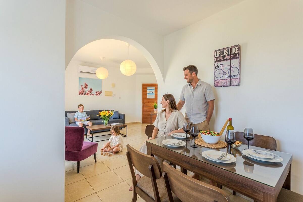 Uma sala de jantar moderna com uma mesa posta para quatro pessoas, um sofá ao fundo e uma parede com uma frase motivacional.