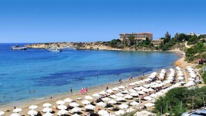 A beach with umbrellas and people, a boat, and buildings in the background. - Artemis Cynthia Complex (Paphos)