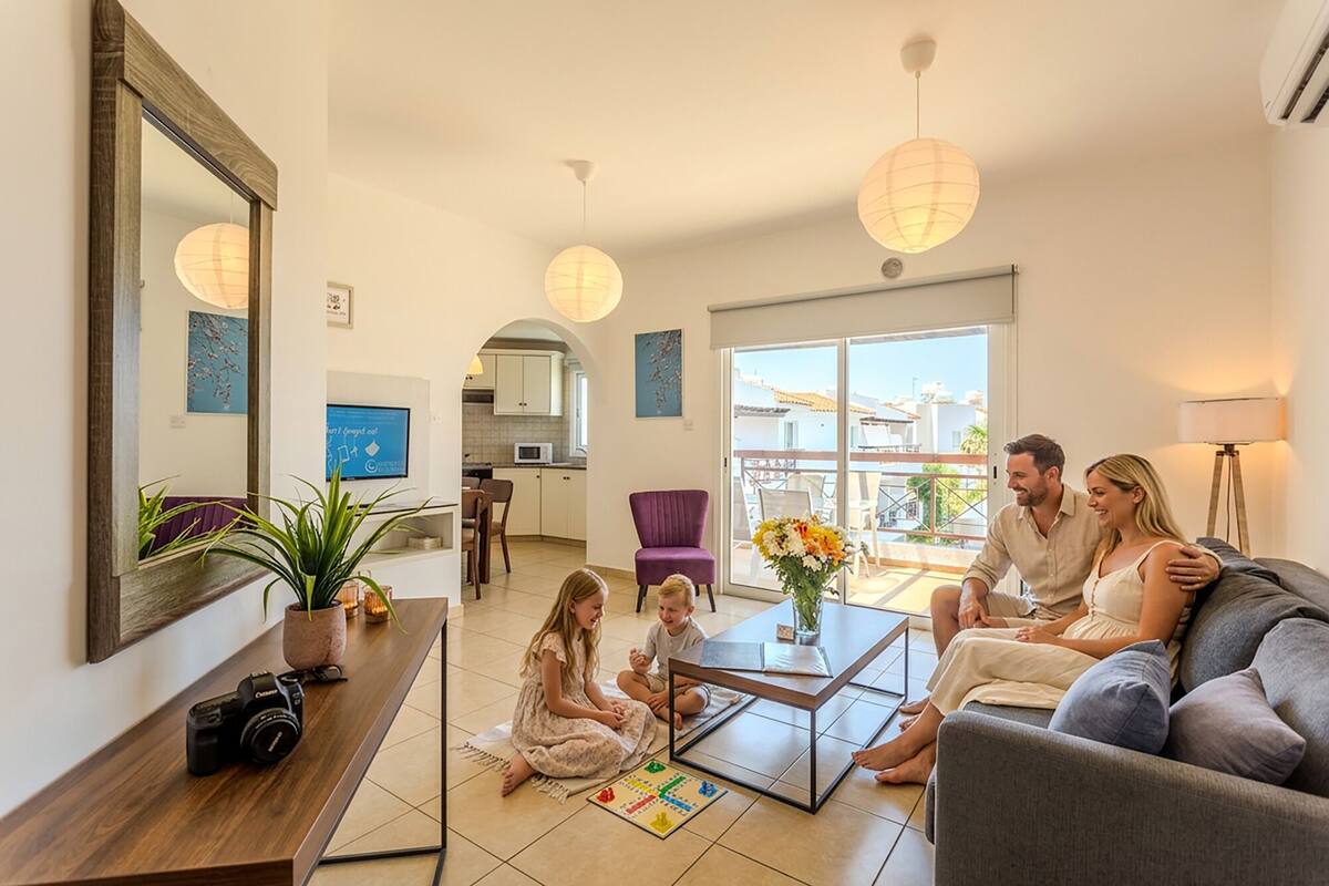 Uma família em uma sala de estar com televisão, mesa de centro e vista para uma varanda.