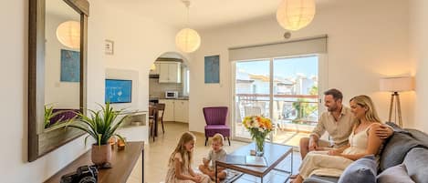 A family in a living room with a TV, a coffee table, and a balcony view.