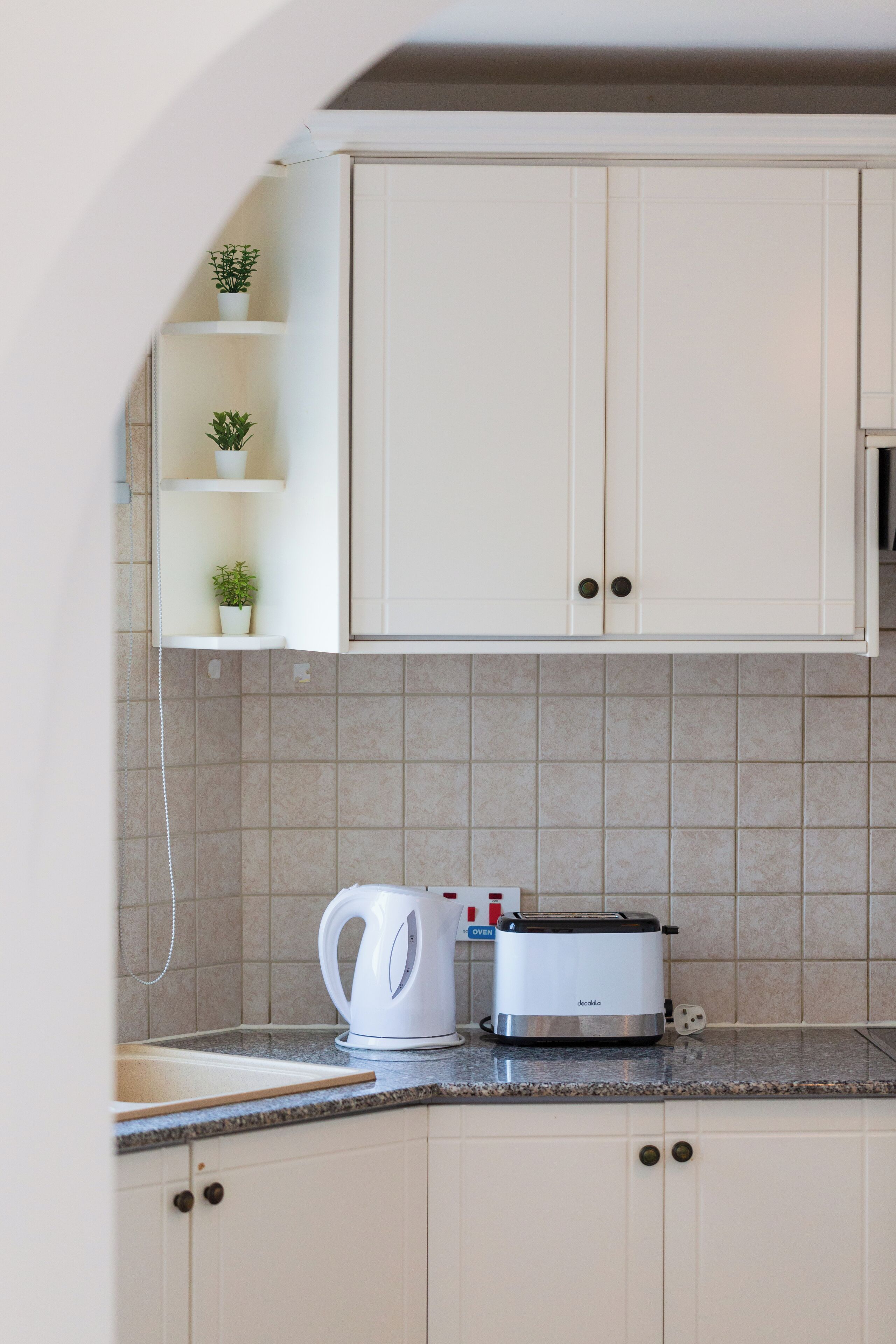 A kitchen with white cabinets, a countertop, a kettle, and a toaster.