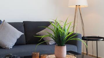 A modern living room with a dark sofa, a glass coffee table, a potted plant, and a floor lamp.