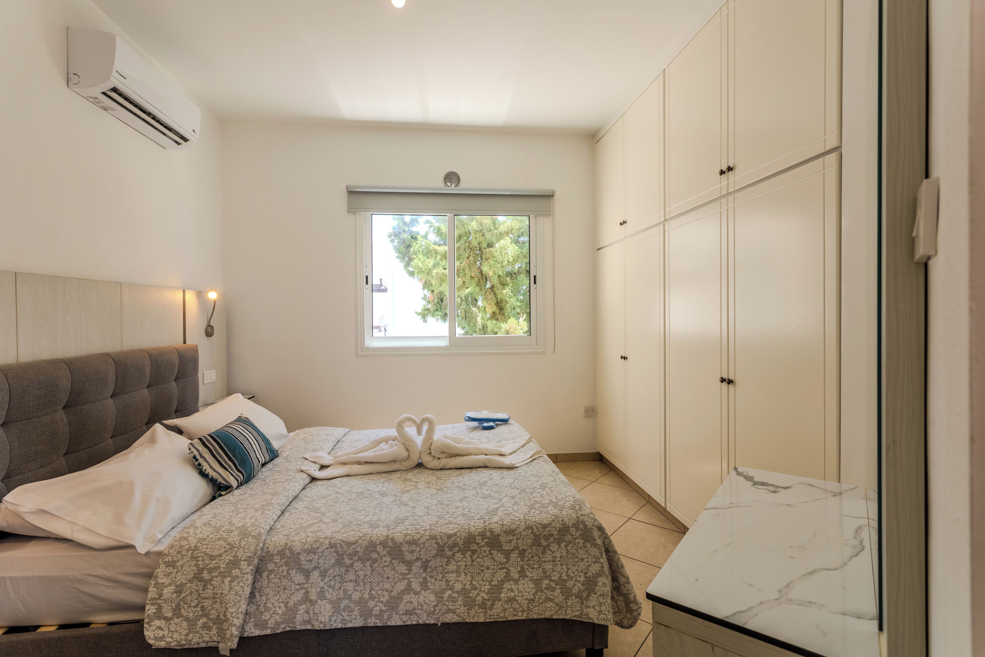 A bedroom with a bed, a window, a wardrobe, and an air conditioning unit.