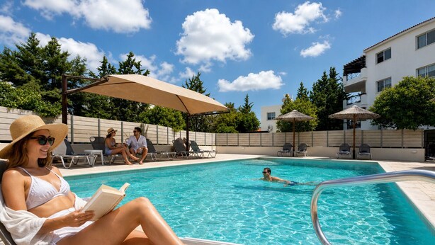 A pool area with lounge chairs, umbrellas, and a clear blue sky. - Artemis Cynthia Complex (Paphos)