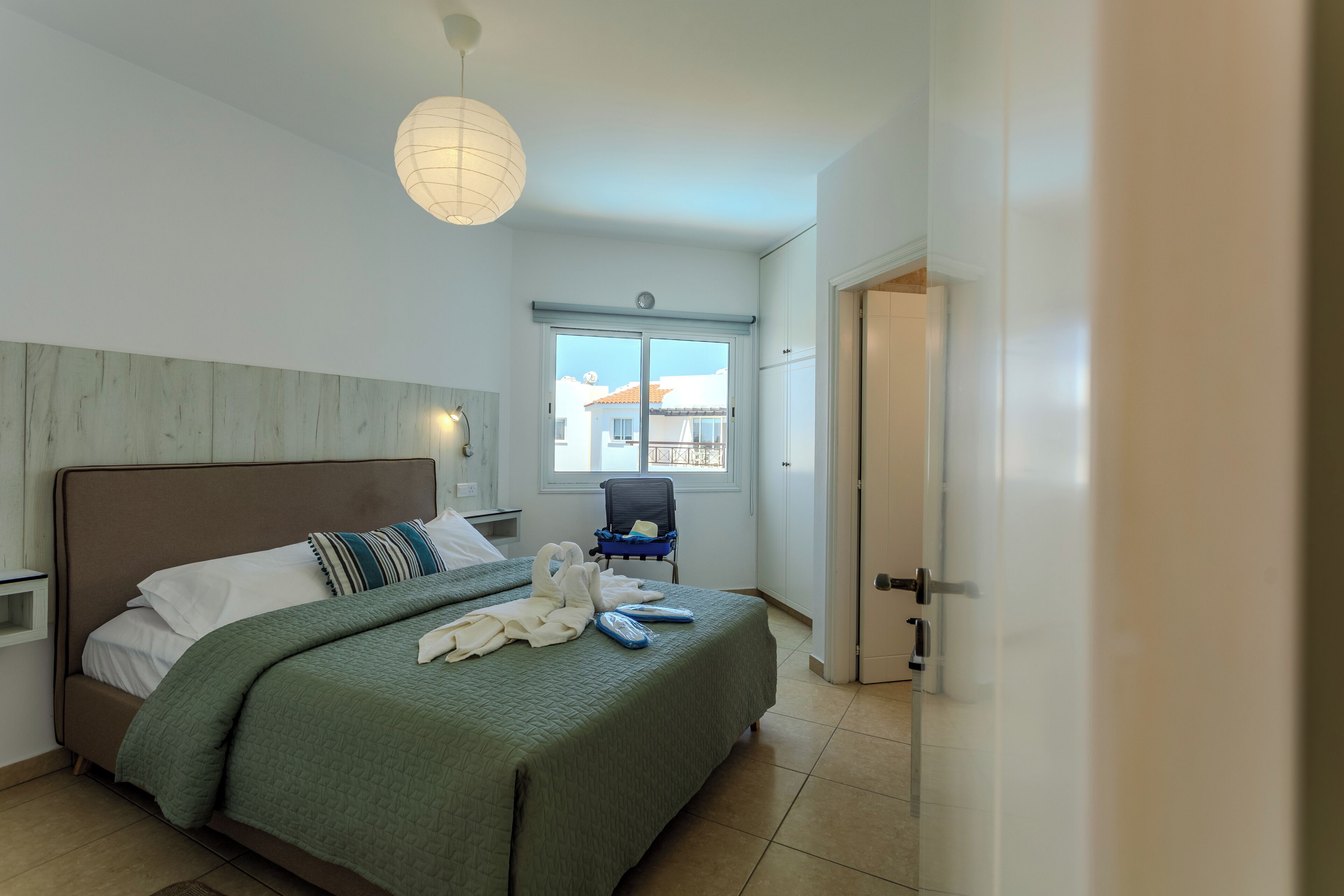 A bedroom with a bed, a nightstand, a lamp, a window with a view, and a door.