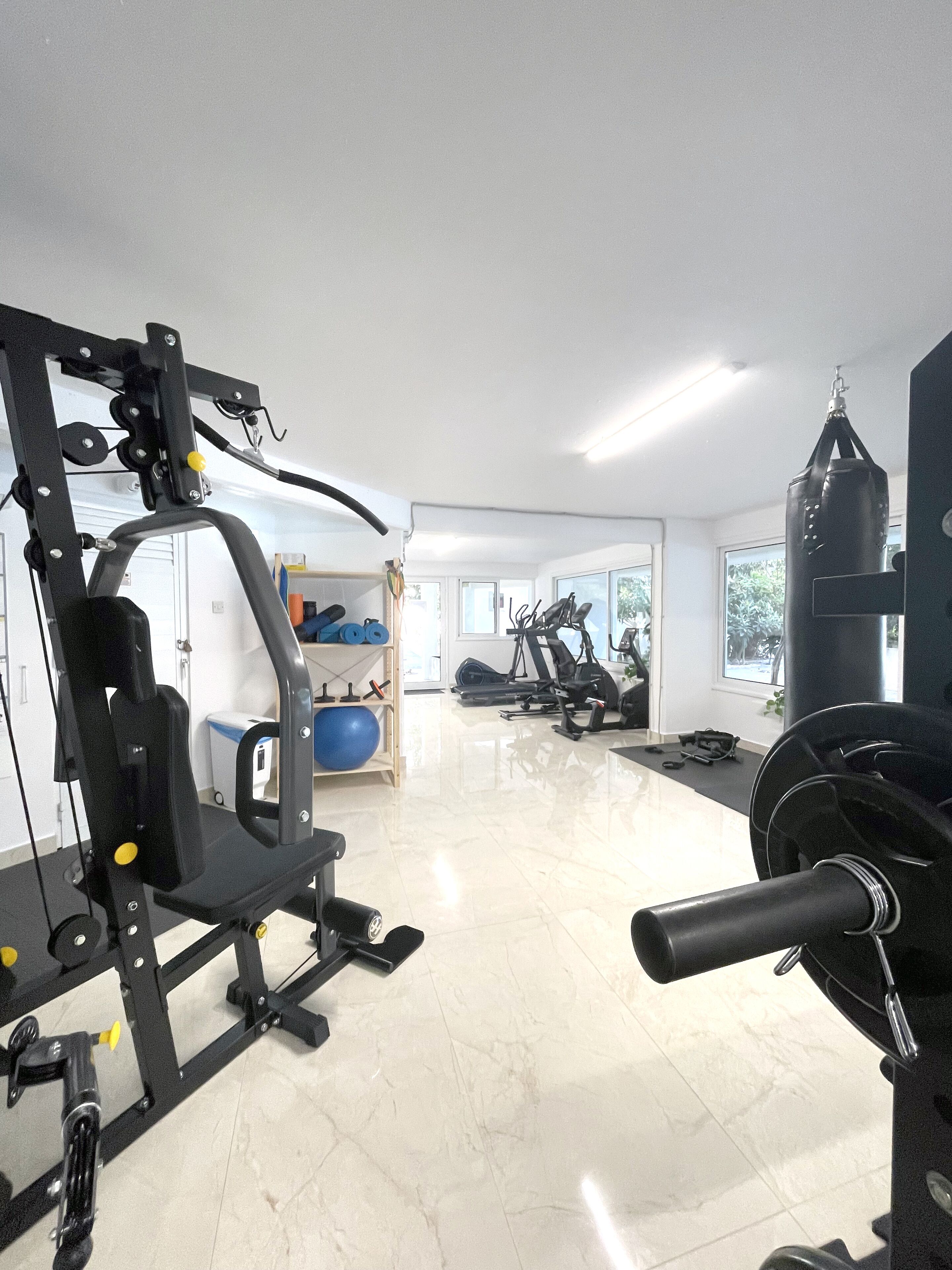 Ein geräumiger Fitnessraum mit verschiedenen Trainingsgeräten, darunter ein Squat-Rack und ein Schlagring.