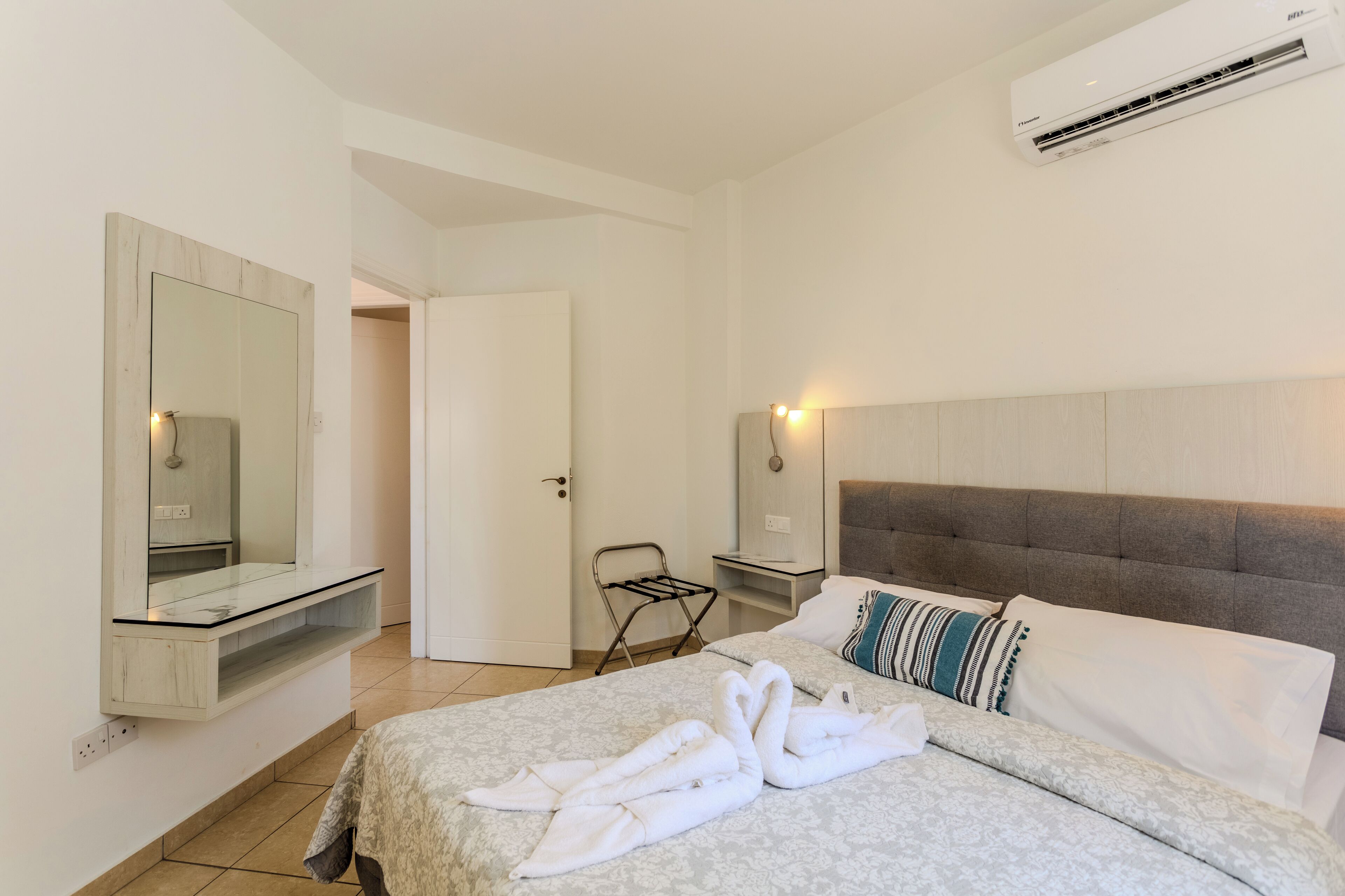 A hotel room with a bed, a mirror, a wall-mounted air conditioner, and a towel rack.