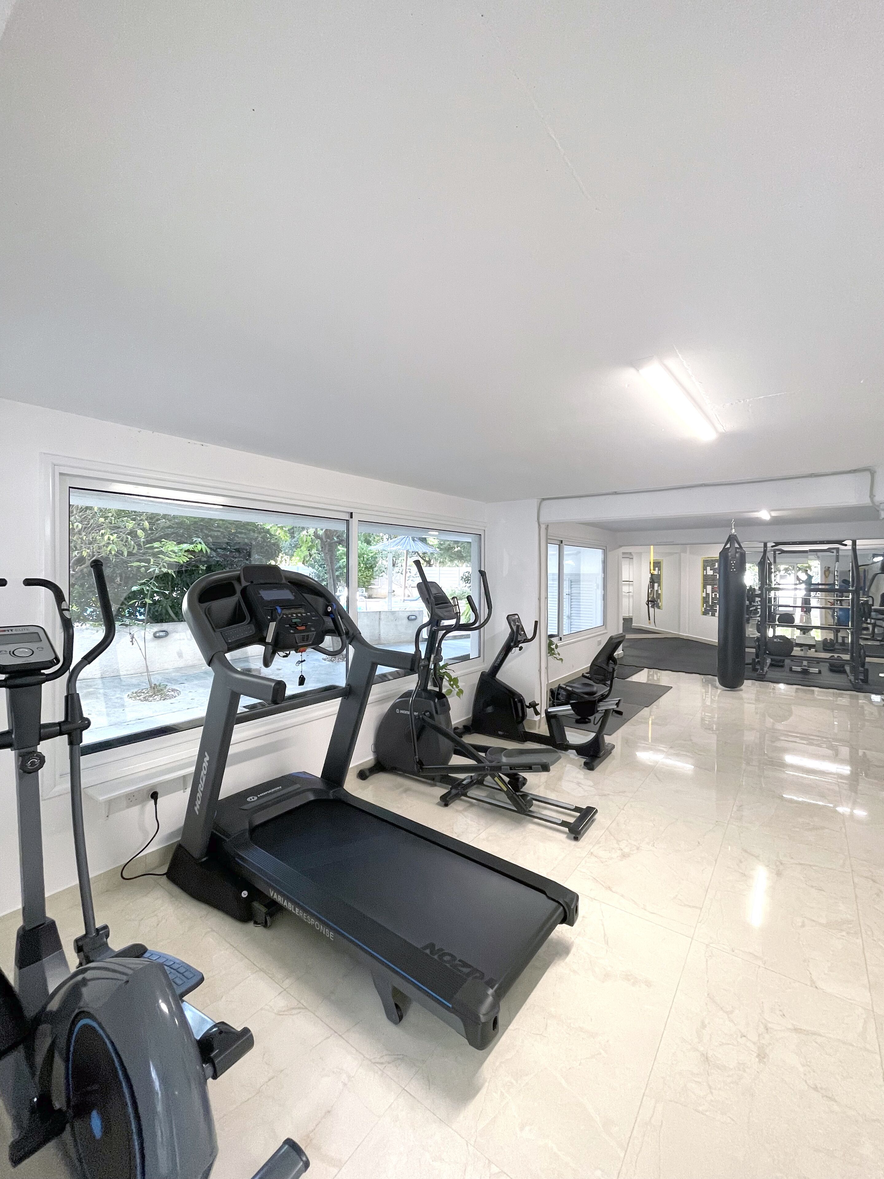Une salle de sport équipée de tapis de course, de vélos elliptiques et d’un sac de frappe.