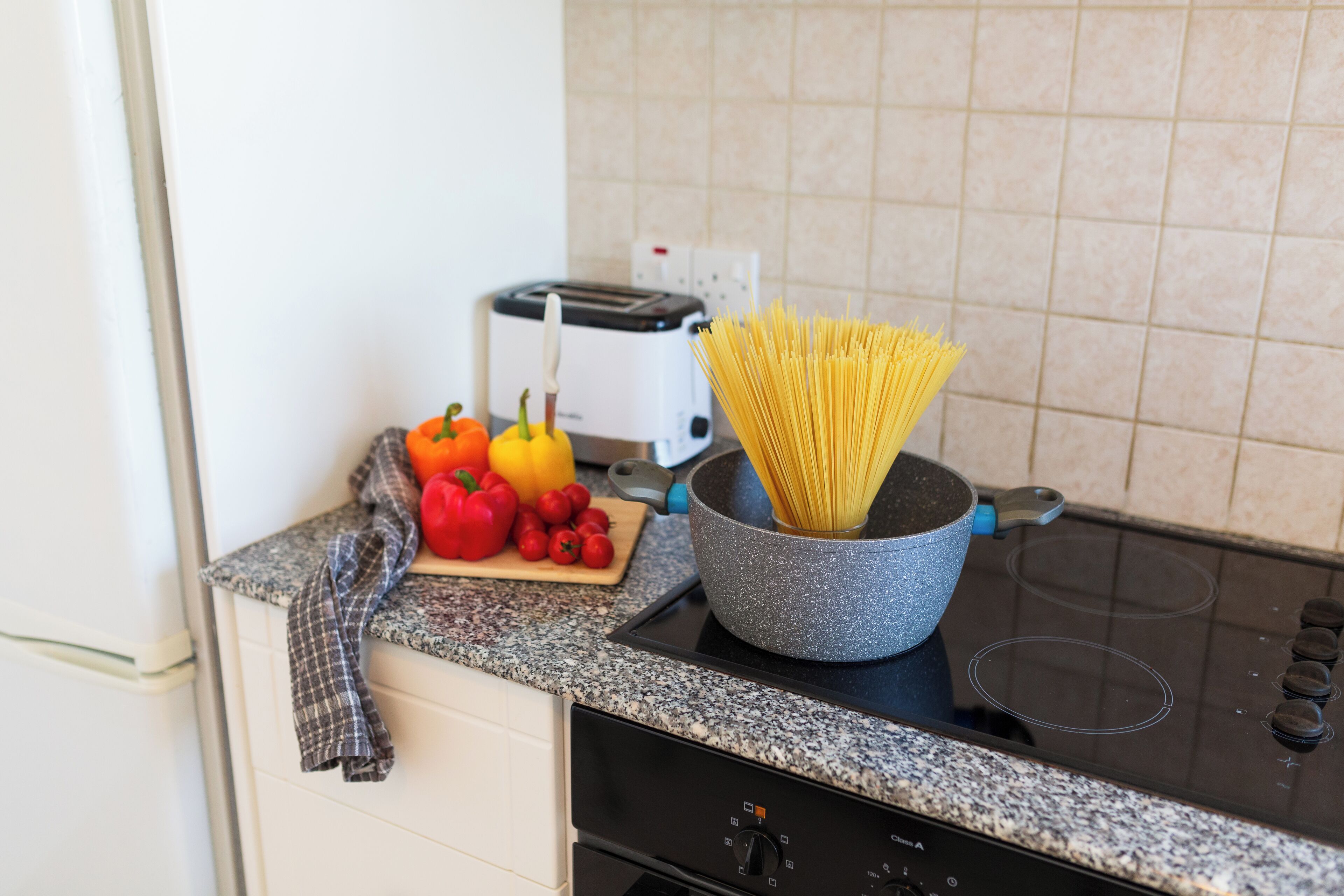 Una cocina con un tostador, una olla de espagueti y una tabla de cortar con verduras.
