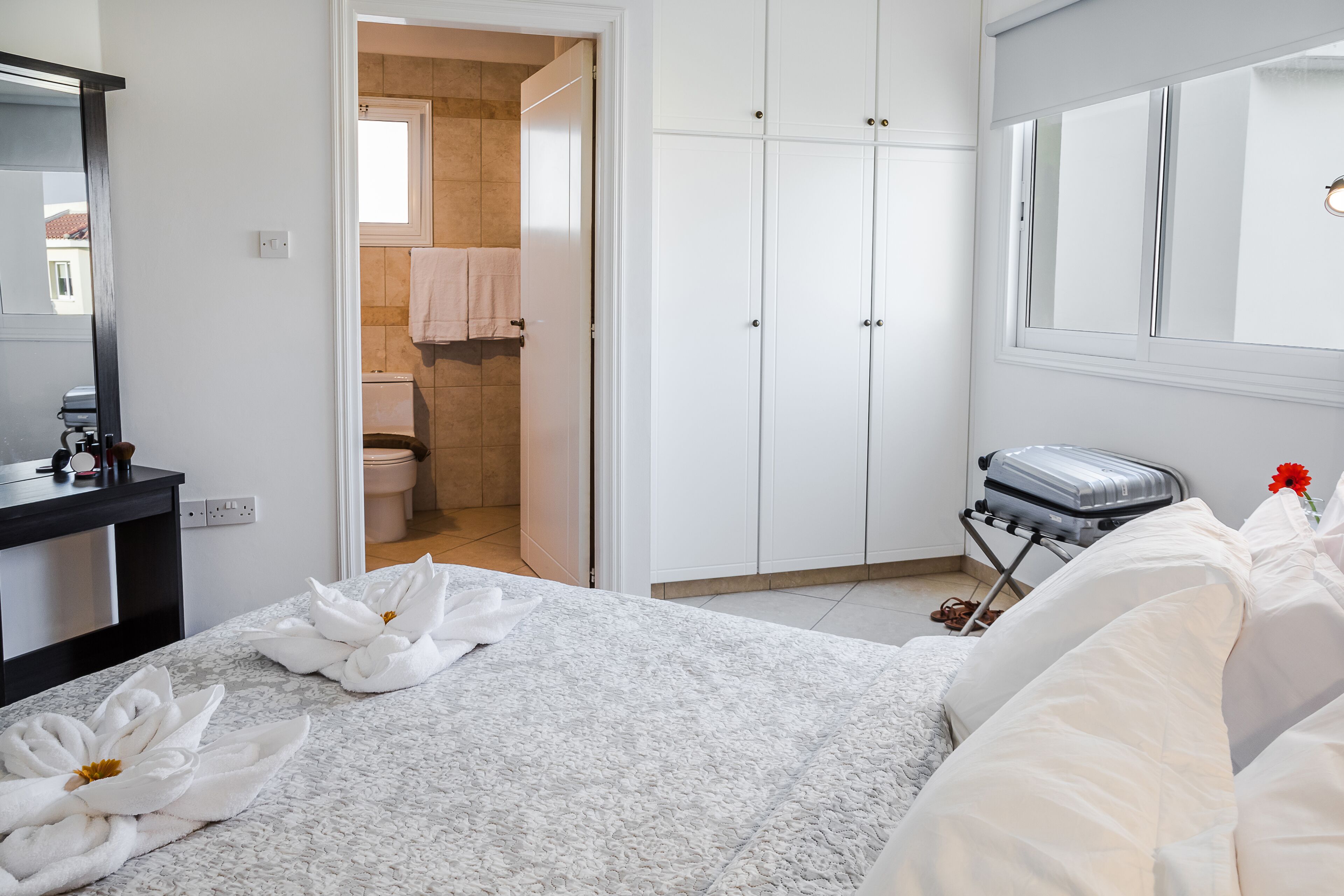 A hotel room with a bed, a suitcase, a bathroom with a towel rack, and a wardrobe.