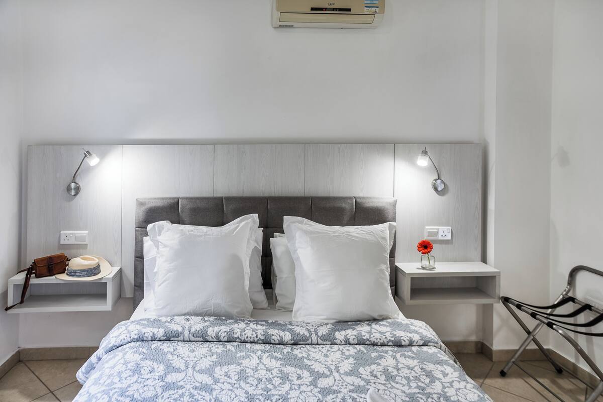 Quarto com cama, duas mesas de cabeceira, ar-condicionado fixado na parede e luminária na parede.