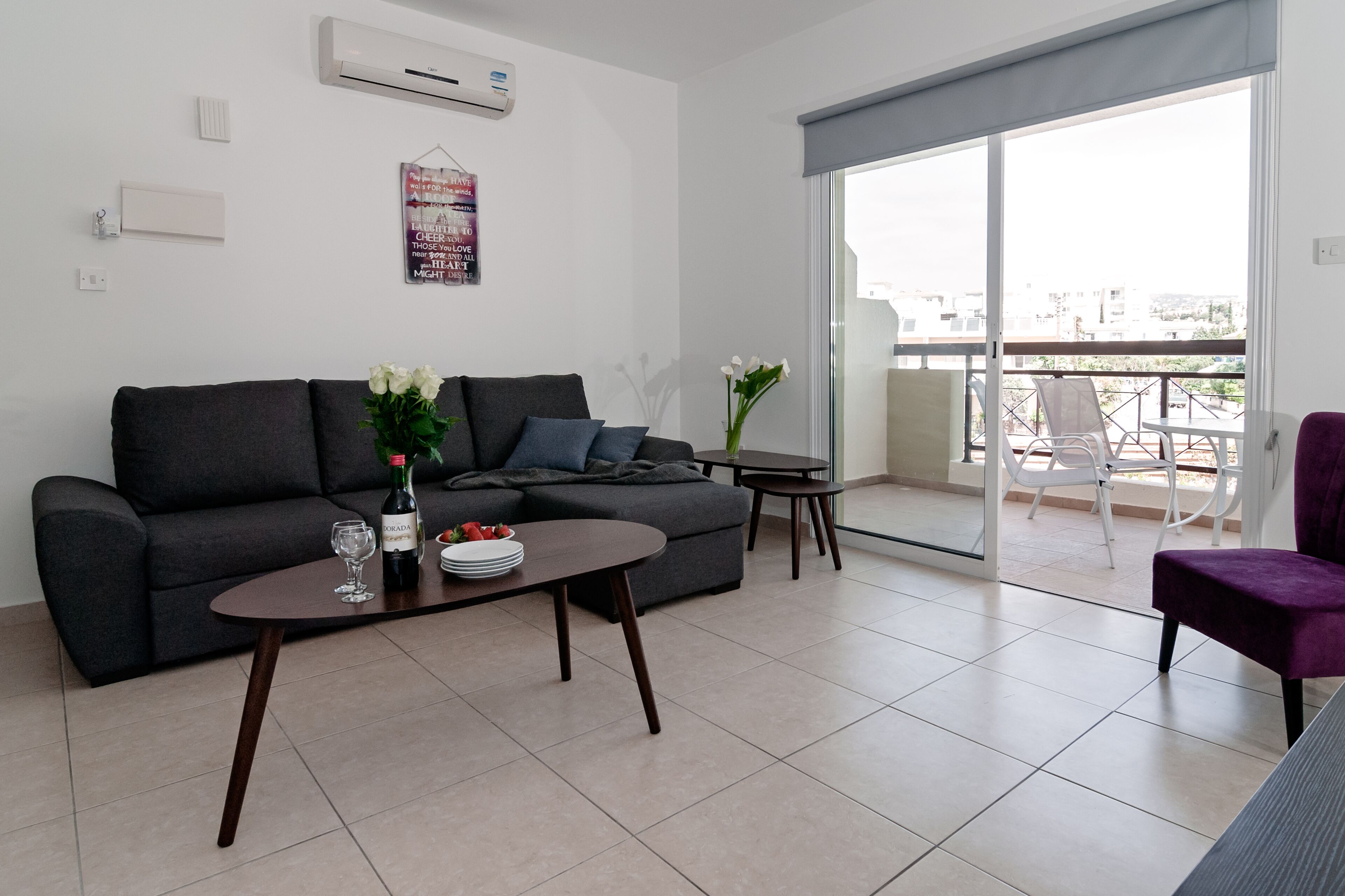 Un soggiorno moderno con un divano grigio, un tavolino da caffè e un tavolo da pranzo. C'è un balcone con vista sulla città.
