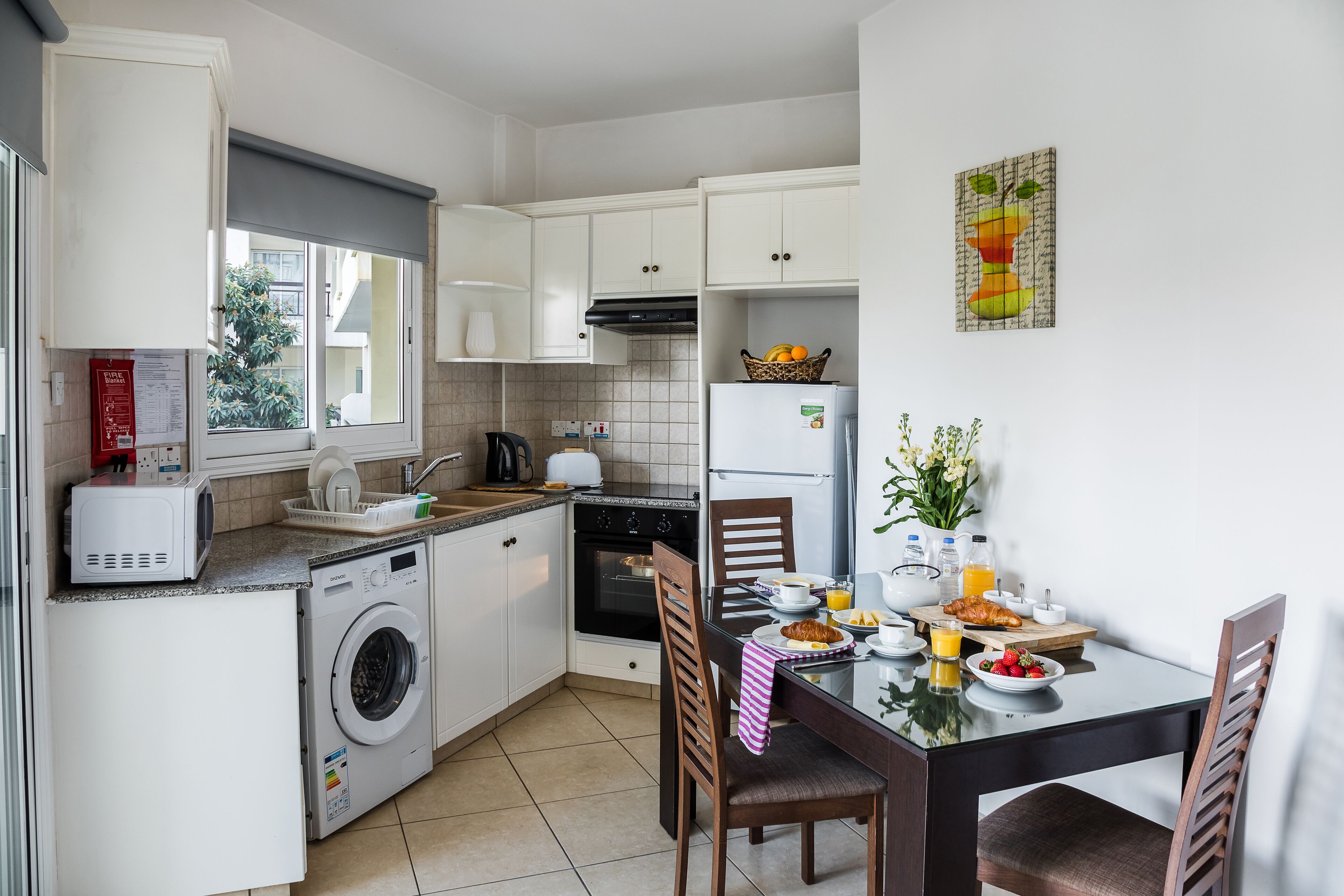 Una cocina compacta con lavadora, refrigerador y comedor con productos para el desayuno.