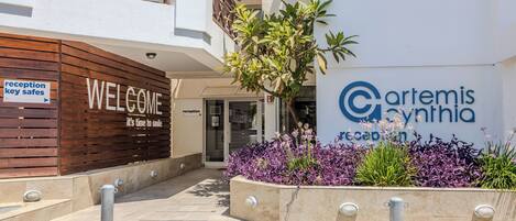 Un área de recepción con un cartel de 'Welcome', mostrador de recepción y un cartel para 'Cartemis Cynthia'.