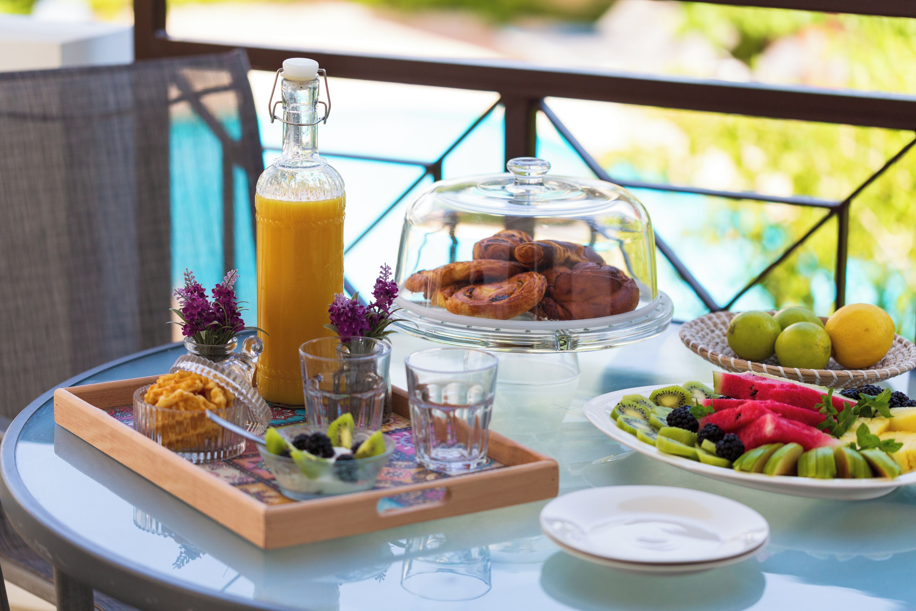 Ein Frühstückstisch mit einer Glasflasche, Gebäck, Früchten und einem Glas Saft.