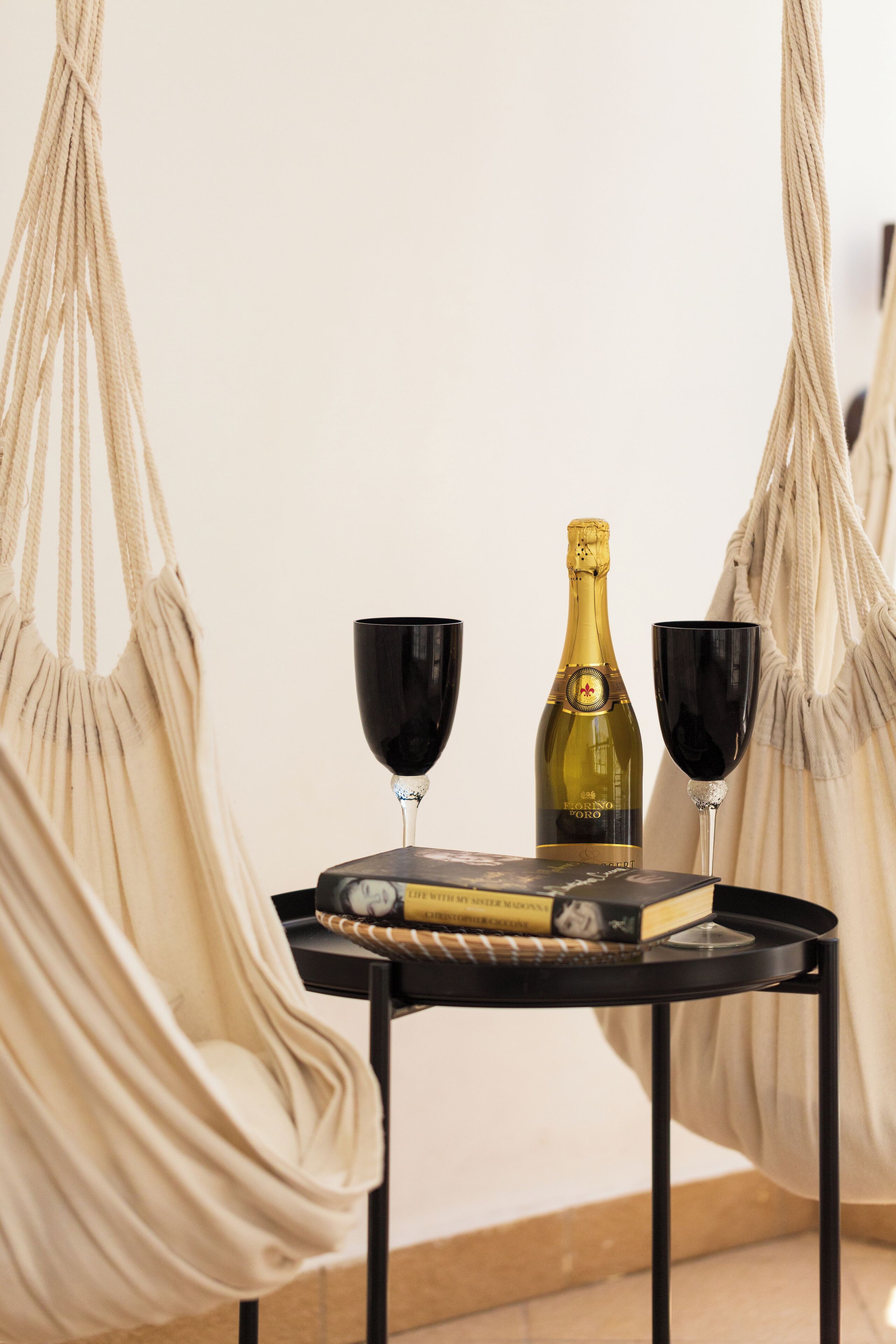 A hammock chair, a small table with a bottle and glasses, and a book.