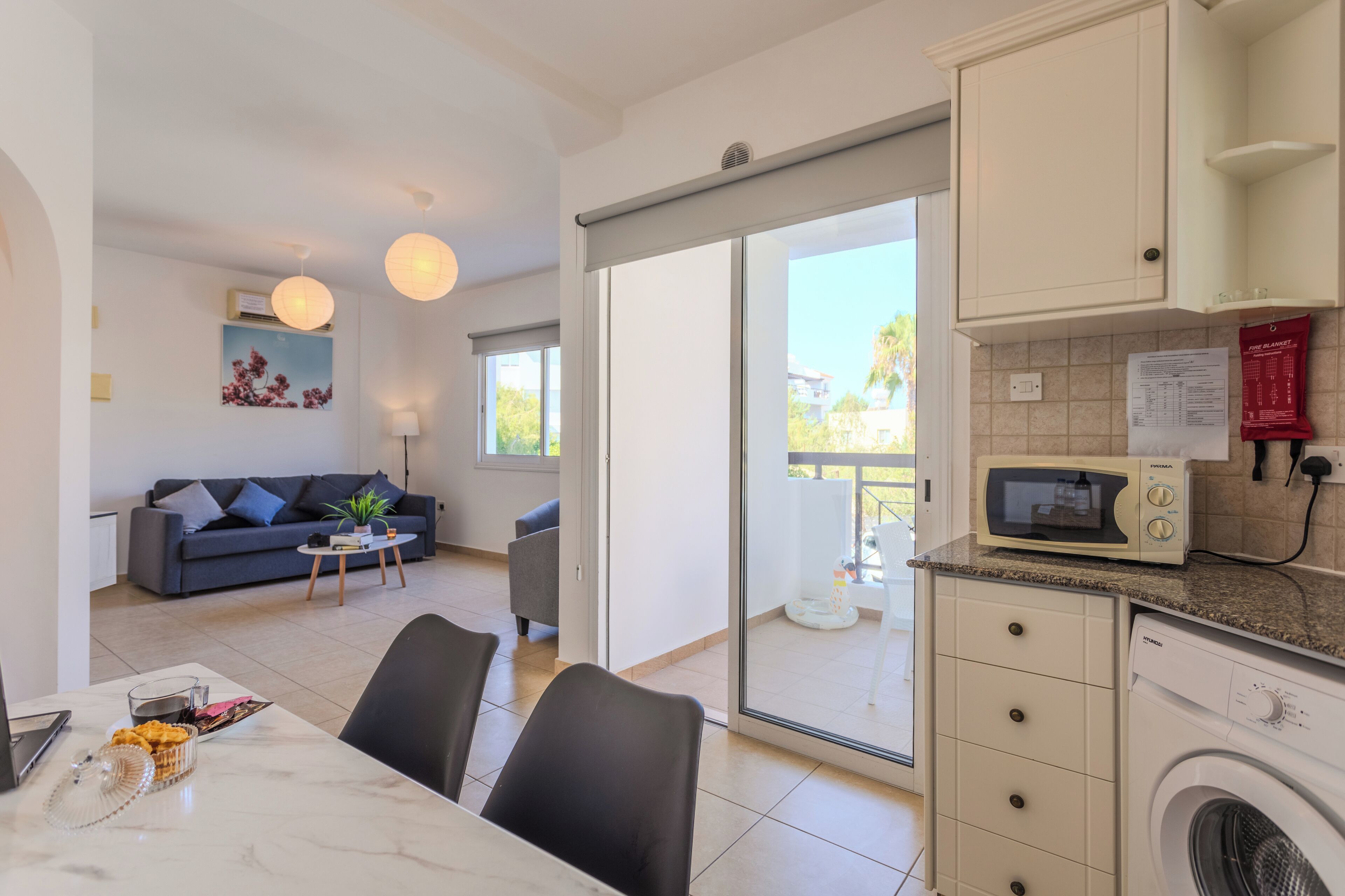 A modern kitchen with a microwave, washing machine, and a dining area with a table and chairs.