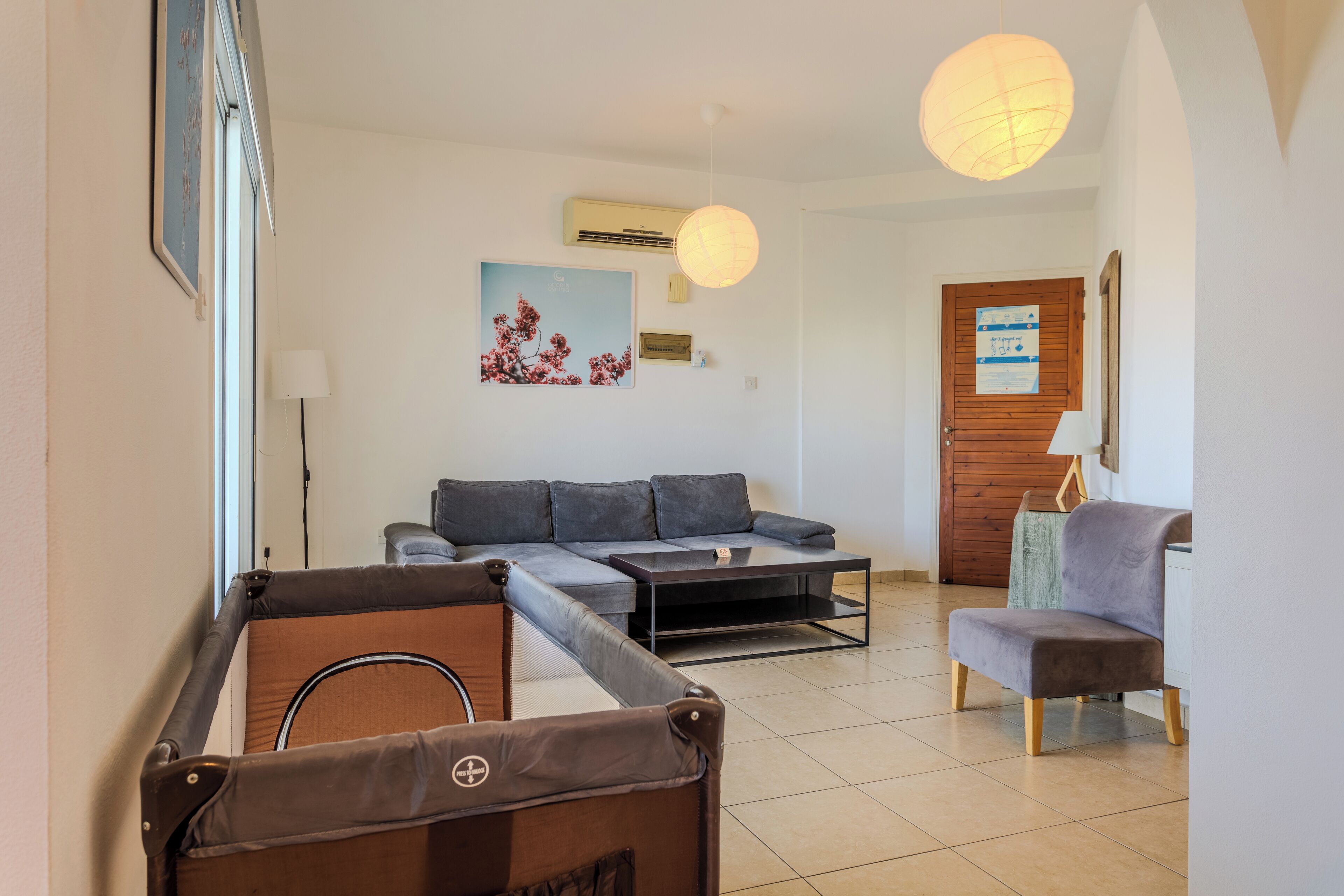 A living room with a sofa, a small table, a chair, a pool table, and a door with a poster.