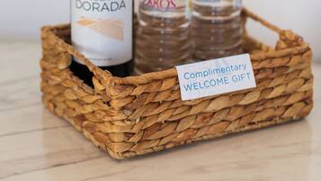 A wicker basket containing a bottle of Vega Dorada wine and two water bottles labeled Zaros. A note on the basket reads "Complimentary Welcome Gift."