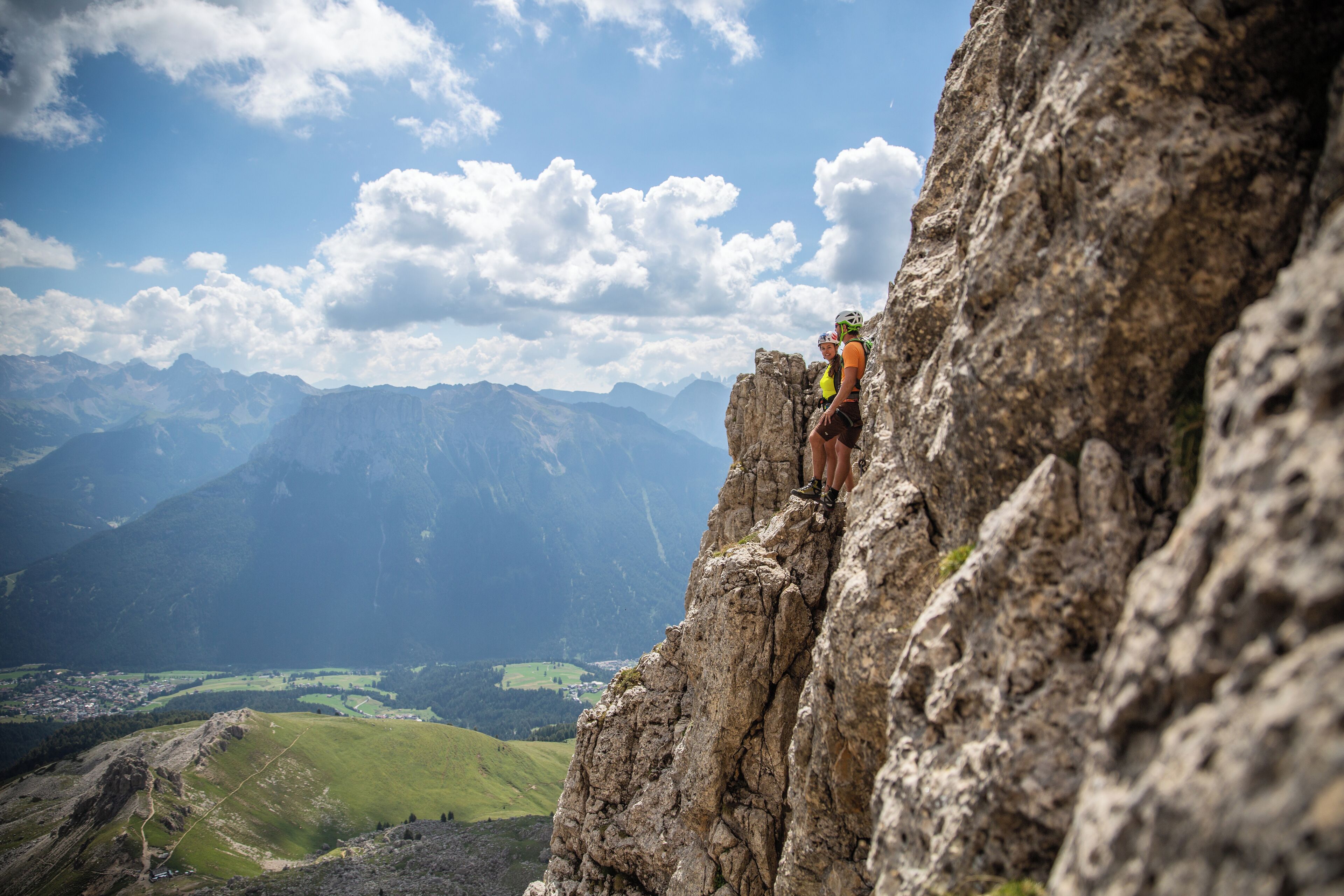 Eine Person erklimmt einen felsigen Bergrücken, im Hintergrund ein Tal und ferne Berge.