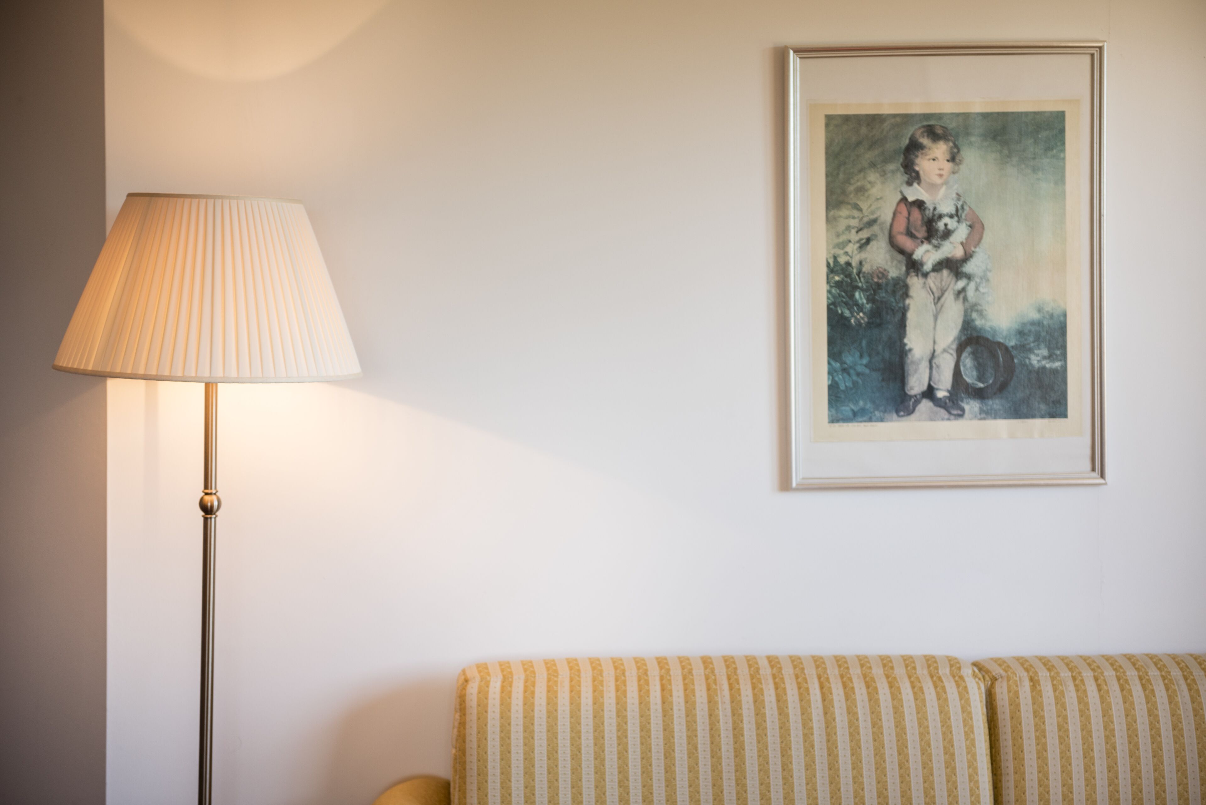 Una habitación con un sofá a rayas, una lámpara de pie y un cuadro en la pared.